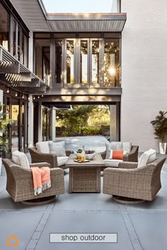 an outdoor patio with wicker furniture and orange throw pillows on the floor, in front of a white brick building