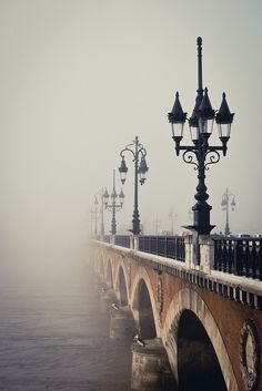 a foggy bridge with street lights and lamps on either side in the foreground