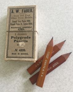 three wooden pencils sitting next to each other on a white surface with an old match card