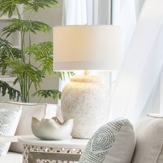 a white table lamp sitting on top of a wooden table next to a vase filled with plants