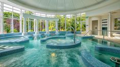 a large indoor swimming pool with blue tile and glass walls, surrounded by windows that look out onto the trees