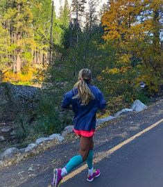 a woman is running down the road with trees in the background