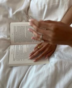 a woman reading a book while laying in bed with her hands on top of the book