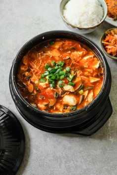 a black bowl filled with food next to bowls of rice