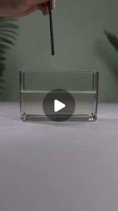 a person is holding a pencil in front of a clear glass container with water inside