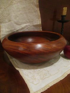 a wooden bowl sitting on top of a table next to an apple and a candle