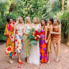 a group of women standing next to each other on a brick floored walkway with palm trees in the background