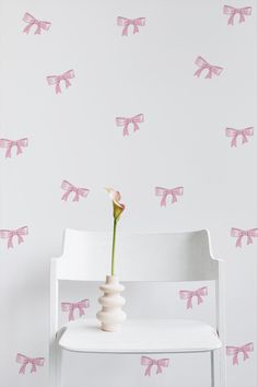 a white chair with a flower in it and pink bows on the wall behind it