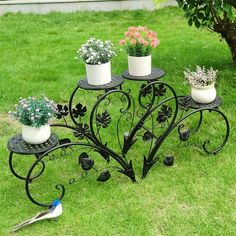 an iron plant stand with three potted plants on it and a bird sitting next to it