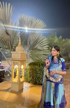 a woman standing in front of a palm tree with her hand up to the camera