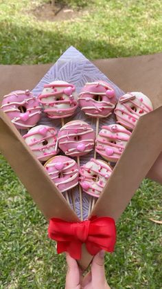 a box filled with pink frosted donuts on top of a grass covered field