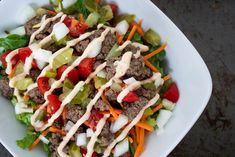 a salad with meat, lettuce and tomatoes in a white bowl on a table