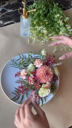 someone is arranging flowers on a plate with greenery in the backgroung