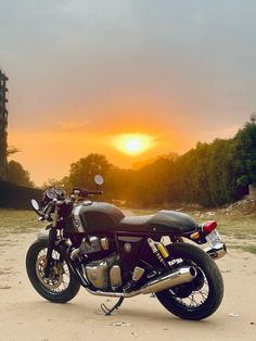 a motorcycle parked on the side of a dirt road at sunset or sunrise with trees in the background