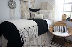 a bed with black and white sheets, pillows and blankets on top of it next to a wicker chair