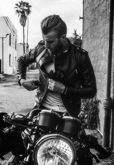 a man sitting on top of a motorcycle next to a brick building with palm trees in the background