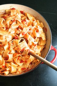 a skillet filled with pasta and sauce on top of a stove next to a wooden spoon