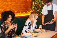 three people sitting at a table with food in front of them and one woman looking at her phone