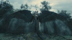 a woman with large black wings standing on top of a rock