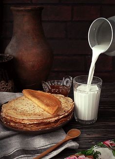 a pitcher pouring milk into a pancake on top of a table next to flowers