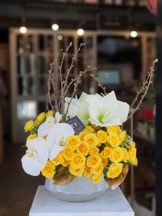 a white vase filled with yellow and white flowers on top of a marble pedestal in front of a store