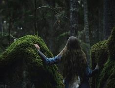 a woman standing in the woods with her arms spread out and moss growing on rocks