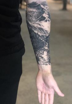 a man's arm with a mountain scene on it and his hand in the air