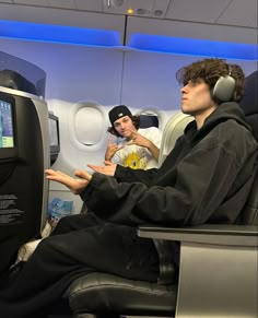 two people sitting on an airplane with headphones in their ears and one person holding his hand out