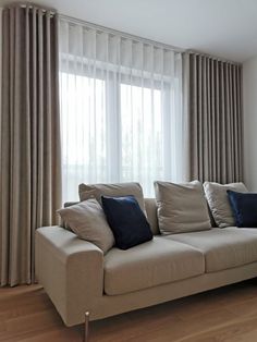 a couch sitting in front of a window next to a wooden floor with two blue pillows on top of it