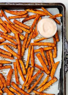 baked sweet potato fries with ranch dressing on a baking sheet, ready to be eaten