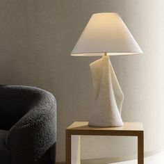 a white lamp sitting on top of a wooden table next to a black chair in a room