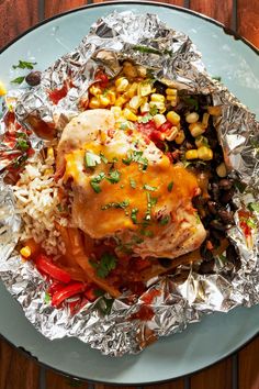 a plate topped with chicken and rice covered in tinfoil on top of a wooden table