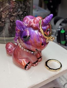 a purple glass figurine sitting on top of a table next to a ring