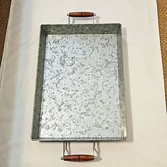 a square metal tray with wooden handles on a white surface