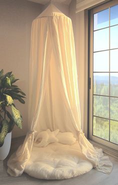 a bed with a white canopy over it next to a potted plant and window