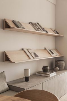 two wooden shelves with books and vases on them in a white living room setting