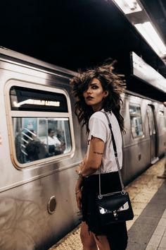 a woman with her hair blowing in the wind while standing next to a subway train