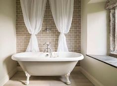 a white bath tub sitting in a bathroom next to a window with drapes on it