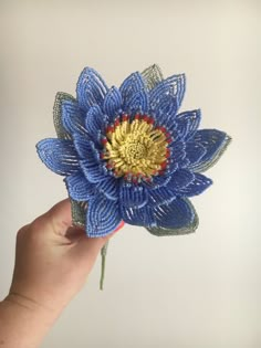 a hand holding a blue flower made out of string and yarn with gold center piece