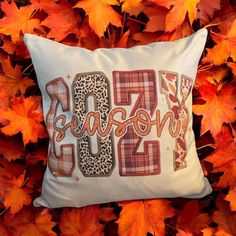 a decorative pillow with the word fall on it in front of autumn leaves and foliage