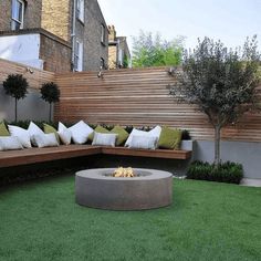 a fire pit in the middle of a lawn with pillows on it and trees near by