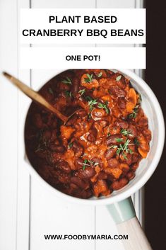 a bowl filled with beans and carrots on top of a white table next to a wooden spoon