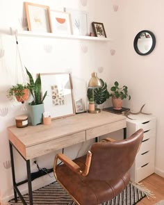 a desk with a chair, potted plants and pictures on the wall above it