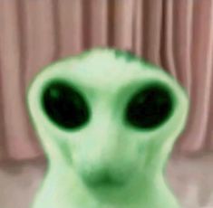 an alien like creature with black eyes and green body, standing in front of curtains