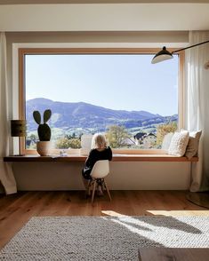 a woman sitting on a chair in front of a window looking out at the mountains