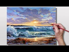 a person is holding a paintbrush in their hand while painting a sunset over the ocean