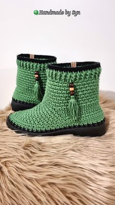 a pair of green crocheted boots sitting on top of a fur rug next to a white wall