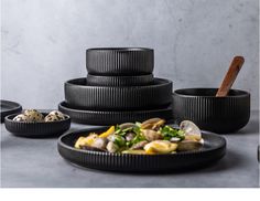 an assortment of bowls and plates with food in them on a gray table top next to a wall