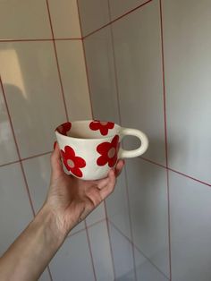 a hand holding a red and white flowered coffee cup in front of a tiled wall