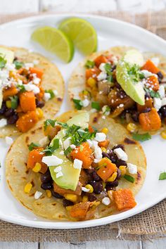 three tortillas with black beans, corn and avocado on a white plate